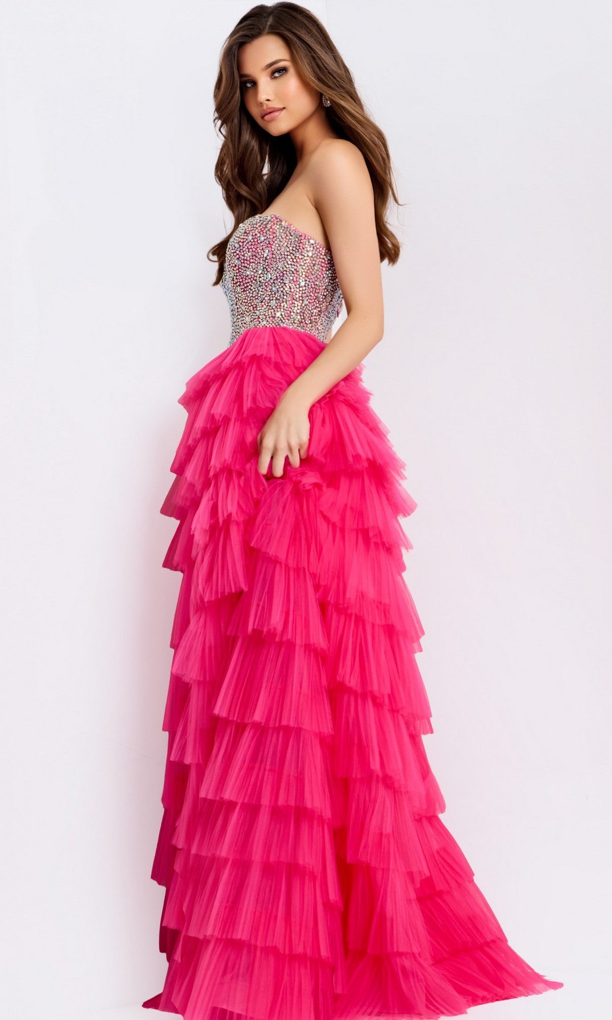 A woman models the Jovani 44360 long prom dress, featuring a strapless rhinestone corset and layered hot pink tulle A-line skirt, against a plain white backdrop.
